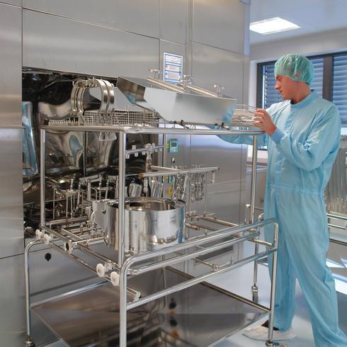 Person in Reinraumkleidung überprüft Edelstahlgeräte in einer sterilen Produktionsumgebung.